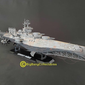 May include: A detailed scale model of the battleship Gustav Dörr, featuring a weathered grey hull with the number 475A printed on the bow. The vessel includes multiple gun turrets, a complex superstructure, and rear propellers, mounted on a black stand.