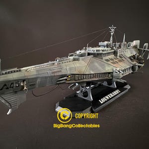 May include: A detailed scale model of a grey battleship with camouflage patterns, featuring the text A45 on the bow and LOEWERHARDT on the base. The vessel includes multiple gun turrets, a bridge structure, and rear propellers, mounted on a black stand.