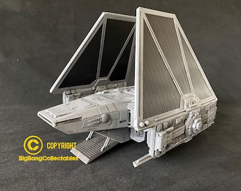 May include: A gray and black model of a Star Wars TIE fighter spaceship. The model has detailed features and is a collectible item.