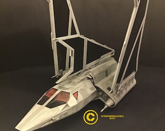 May include: A gray and black spaceship model with a long, pointed nose and two large, angled wings. The wings are made of a black, grid-like material. The model is sitting on a black surface. COPYRIGHT BIGRANGE COLLECTIBLES ON ETSY