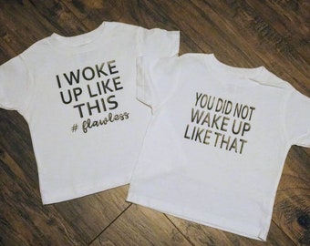 May include: Two white t-shirts with gold lettering. The first shirt says "I woke up like this #flawless". The second shirt says "You did not wake up like that".