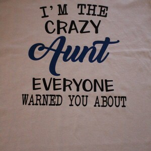 May include: White t-shirt with black text that reads "I'm the crazy Aunt everyone warned you about". The word "Aunt" is in blue cursive.