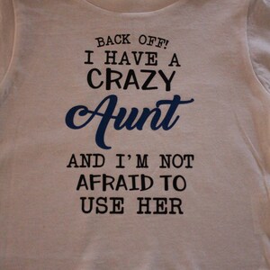 May include: White t-shirt with black text that reads "Back off! I have a crazy Aunt and I'm not afraid to use her."