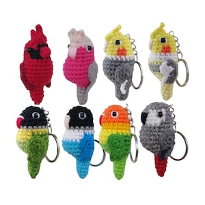 May include: A set of eight crocheted bird keychains. The keychains are in various colors, including red, pink, yellow, gray, green, blue, and orange. Each keychain features a small crocheted bird with a key ring attached.