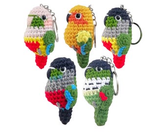 May include: Five handmade crochet parrot keychains in various colors, including pink, yellow, green, and blue. Each keychain features a silver metal ring for attaching to keys or bags. The parrots have detailed features and vibrant colors.