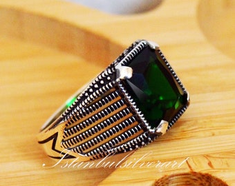 May include: A silver ring with a green gemstone. The ring has a detailed design with a textured band.