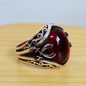 May include: A silver ring with an ornate design and a large, red gemstone.