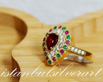 May include: A gold ring featuring a red heart-shaped stone surrounded by smaller white and green stones.