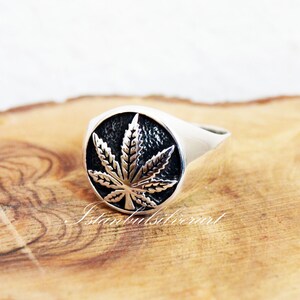 Puede incluir: Un anillo de plata con un dise&ntilde;o detallado de hoja de marihuana. El anillo es redondo y tiene un acabado liso y pulido.