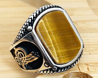 May include: A silver ring with a large, rectangular, golden tiger's eye stone. The ring has a detailed design on the band.