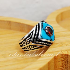 May include: A silver ring with a turquoise and red stone inlay. The ring has an intricate design with swirls and lines.