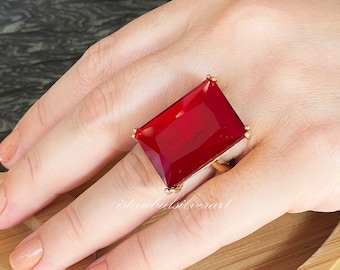 May include: A gold ring with a large, rectangular, red gemstone. The ring is worn on a finger.
