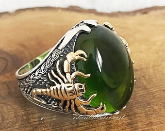 Puede incluir: Un anillo de plata con una piedra preciosa verde y un diseño de escorpión dorado.