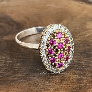 Puede incluir: Un anillo de plata con un engaste de forma ovalada. El engaste está lleno de pequeñas piedras rosas y blancas.