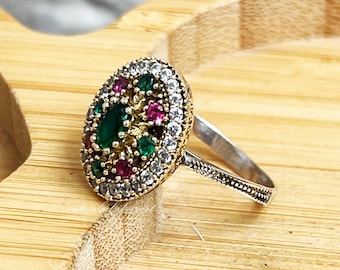 Può includere: Un anello d'argento con una montatura ovale che presenta una pietra preziosa verde e rosa circondata da pietre bianche più piccole.