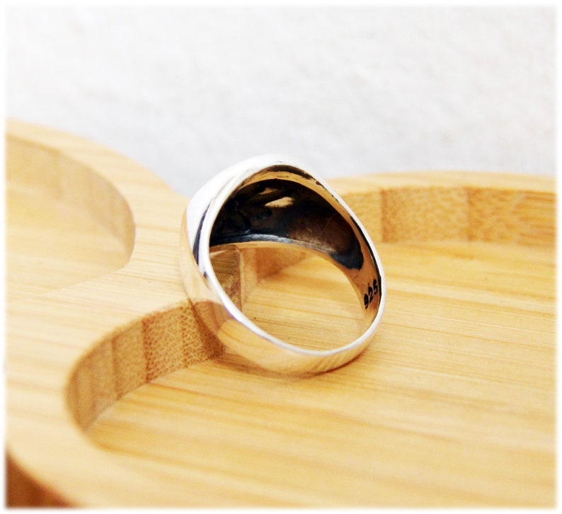 Puede incluir: Un anillo de plata con la parte superior redondeada y un acabado liso y pulido. El anillo est&aacute; sobre una superficie de madera.
