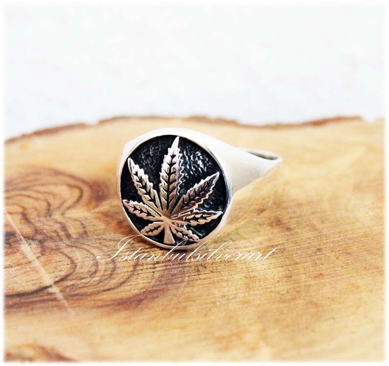Puede incluir: Un anillo de plata con un dise&ntilde;o detallado de hoja de marihuana. El anillo es redondo y tiene un acabado liso y pulido.