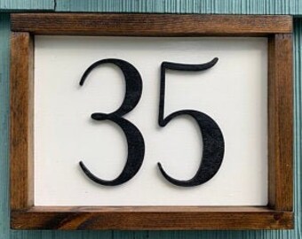 May include: A white wooden sign with a brown wood frame, featuring the number 35 in black.