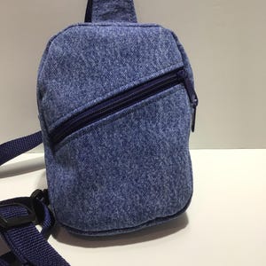 May include: A small blue denim crossbody bag with a zippered pocket and a blue adjustable strap.