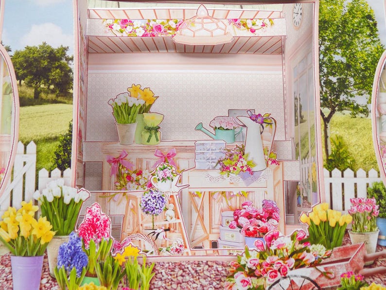 May include: A papercraft diorama of a flower shop, featuring a variety of colorful paper flowers, including tulips, daffodils, and hyacinths. The scene includes a watering can, a white picket fence, and a decorative cart, all in pastel colors.