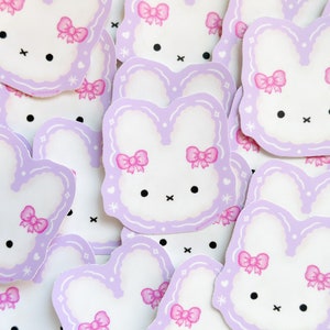 May include: A collection of purple and white bunny stickers with pink bows. The stickers have a simple, cartoon-like design.
