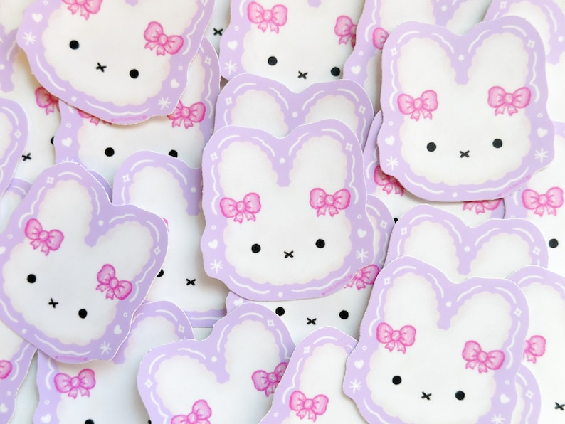 May include: A collection of purple and white bunny stickers with pink bows. The stickers have a simple, cartoon-like design.