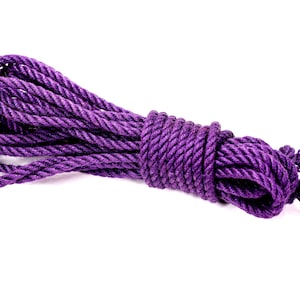 May include: A bundle of thick, twisted rope in a vibrant purple hue. The rope is tightly wound in the center and has loose ends, suggesting it's ready for use. The background is plain white, highlighting the rope's texture and color.