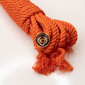 May include: A close-up of a bright orange cotton rope, coiled and ready for use. The rope is thick and has a slightly frayed texture.