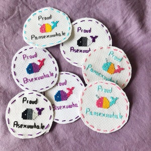 Puede incluir: Siete parches bordados con un diseño de ballena y el texto "Proud" y una etiqueta de orientación sexual diferente en cada uno. Las etiquetas son "Pansexualwhale", "Asexualwhale", "Bisexualwhale" y "Pansexualwhale".