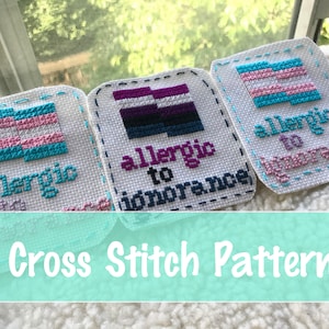 May include: Cross stitch pattern featuring three embroidered patches. Each patch has a white background with a different LGBTQ+ flag design and the words "allergic to ignorance". The text "Cross Stitch Pattern" is at the bottom.