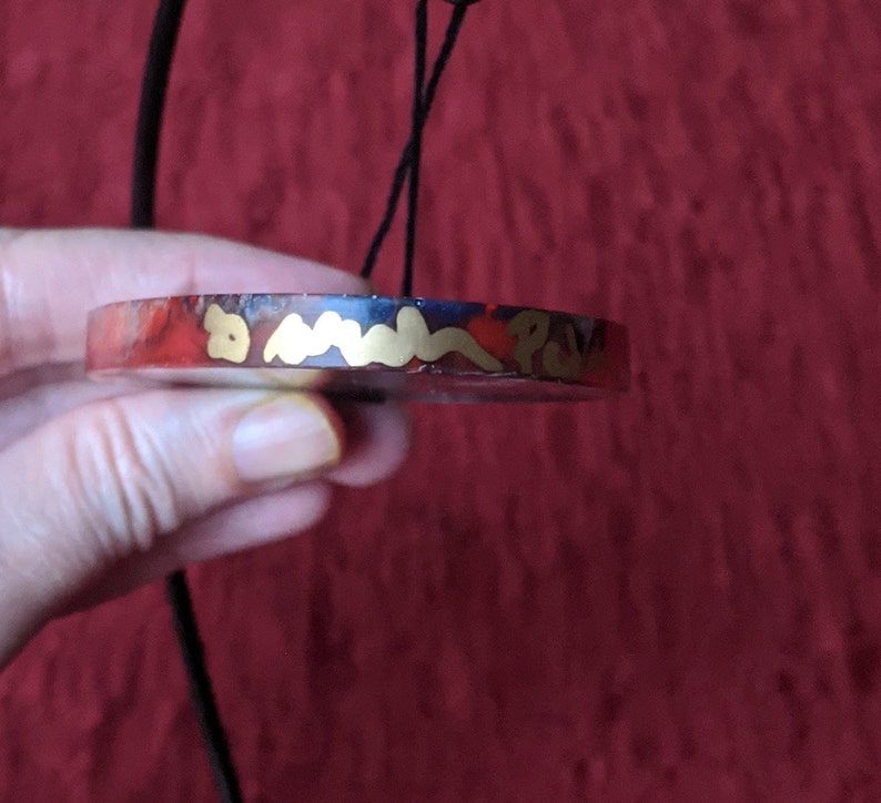 Unique red and blue hand made resin flow art oval ornament on a metal display white