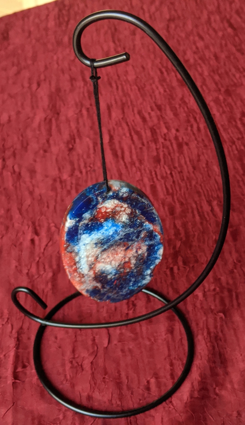 Unique red and blue hand made resin flow art oval ornament on a metal display white