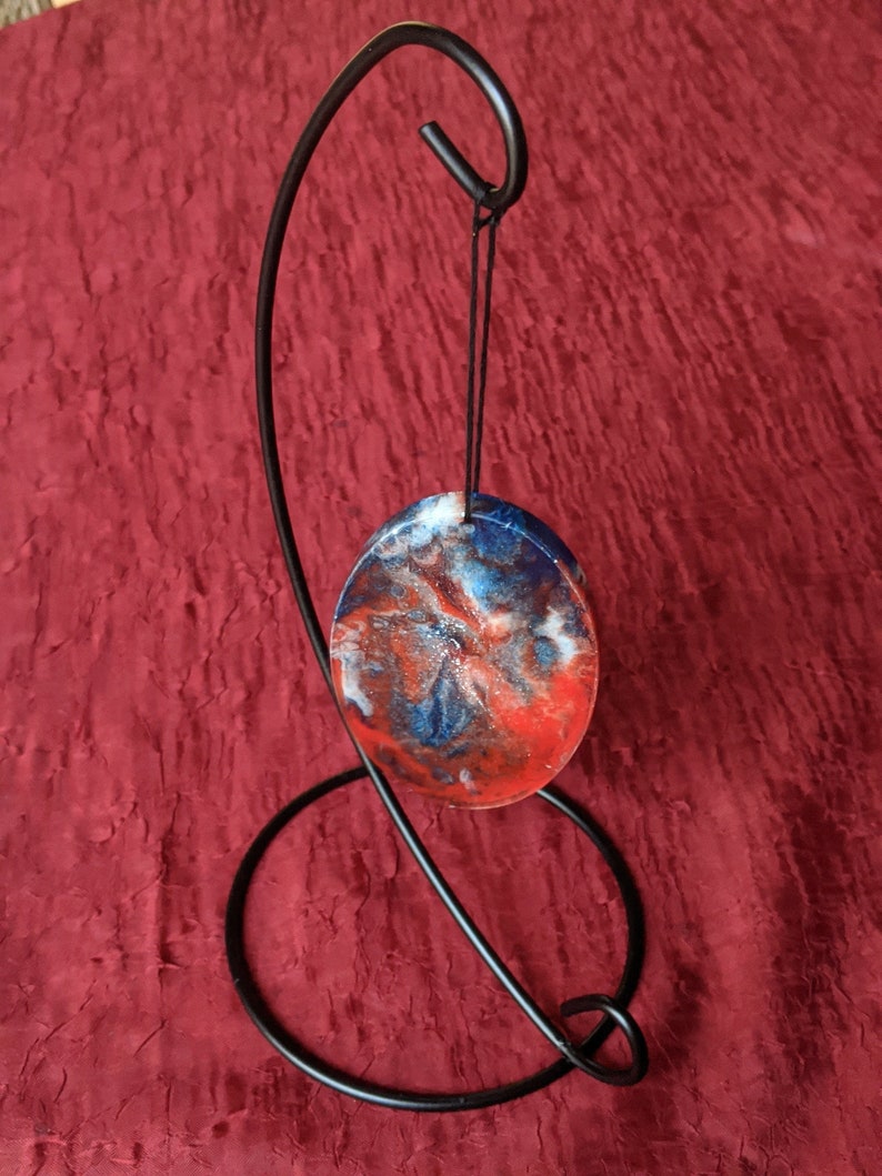 Unique red and blue hand made resin flow art oval ornament on a metal display white