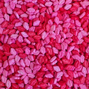 Könnte beinhalten: Ein Nahaufnahmebild von rosa und roten lippenförmigen Streuseln. Die Streusel sind perfekt zum Dekorieren von Kuchen, Cupcakes und anderen Desserts.