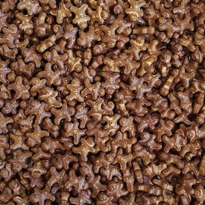 May include: A close-up image of a large quantity of brown gingerbread man sprinkles. The sprinkles are small and have a slightly shiny finish.