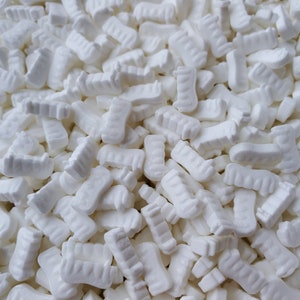 May include: A close-up image of a pile of white packing peanuts. The peanuts are shaped like small, irregular blocks with a textured surface.