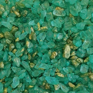 May include: An overhead shot of a collection of teal and gold-colored, irregularly shaped stones. The stones are scattered across the frame, creating a textured, natural appearance. The teal stones are translucent, and the gold stones are opaque.