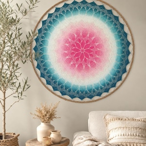 May include: A large circular wall hanging featuring an intricate crochet mandala pattern. The design transitions from a vibrant pink centre to a soft white middle, ending in a deep teal outer edge, all secured within a circular wooden frame.