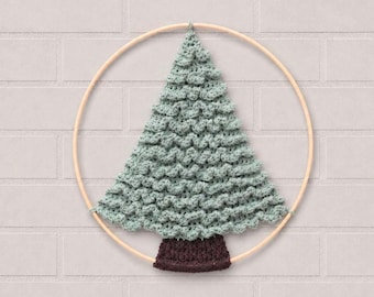 May include: A wall hanging featuring a light green crocheted Christmas tree with a textured bobble stitch pattern, attached to a circular wooden hoop. The tree has a dark brown crocheted trunk at the base, secured to the bottom of the wooden frame.