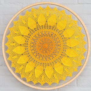 May include: A handcrafted, yellow and orange crochet dream catcher in the shape of a sunflower. The sunflower design is centered within a natural wood hoop. The crochet work features detailed petal and center patterns, creating a decorative wall hanging.