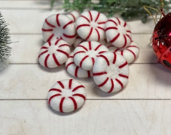Puede incluir: Un grupo de caramelos de menta de fieltro en rojo y blanco, dispuestos sobre una superficie de madera blanca.