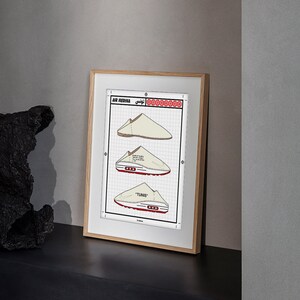 May include: Framed print featuring three illustrations of a shoe design labeled "AIR MEDINA TUNIS". The drawings are in beige and red on a grid background, with text in English and Arabic. The frame is light wood.