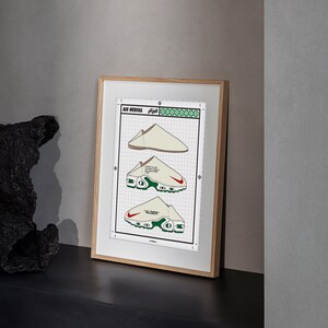 May include: Framed print featuring three illustrations of a white and red sneaker design. The print includes the text "AIR MEDINA" and "ALGER" along with Arabic script. The sneakers have green and red accents and are set against a grid background.