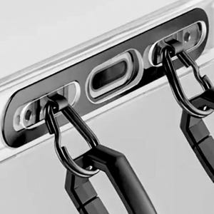 Może przedstawiać: Zbliżenie przezroczystego etui na telefon z czarną ramką i dwoma czarnymi karabińczykami. Etui ma wycięcia na aparat i port ładowania telefonu. Karabińczyki są przeznaczone do mocowania do smyczy lub paska.