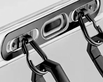 May include: Close-up of a clear phone case with a black frame and two black carabiner clips attached. The case has cutouts for the phone's camera and charging port. The carabiners are designed to attach to a lanyard or strap.