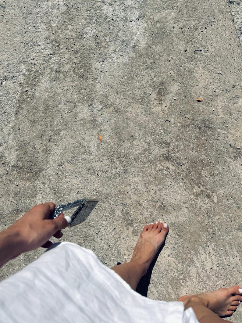 A person wearing a white dress and holding a silver phone chain with a case attached.