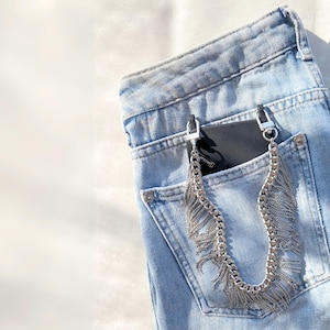 Silver fringe chain phone strap attached to black phone case on a blue jean