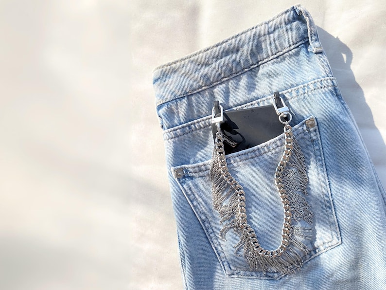 Silver fringe chain phone strap attached to black phone case on a blue jean