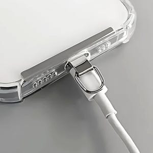 May include: Transparent phone case with a silver metal detail and a white charging cable connected. The case allows the phone's colour to be seen. The cable is plugged into the phone.