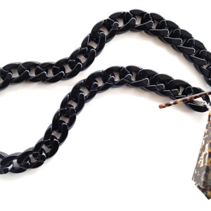 Peut inclure: Une chaîne en plastique noire avec un design de maillons épais. La chaîne est attachée à une paire de lunettes de soleil en écaille de tortue.